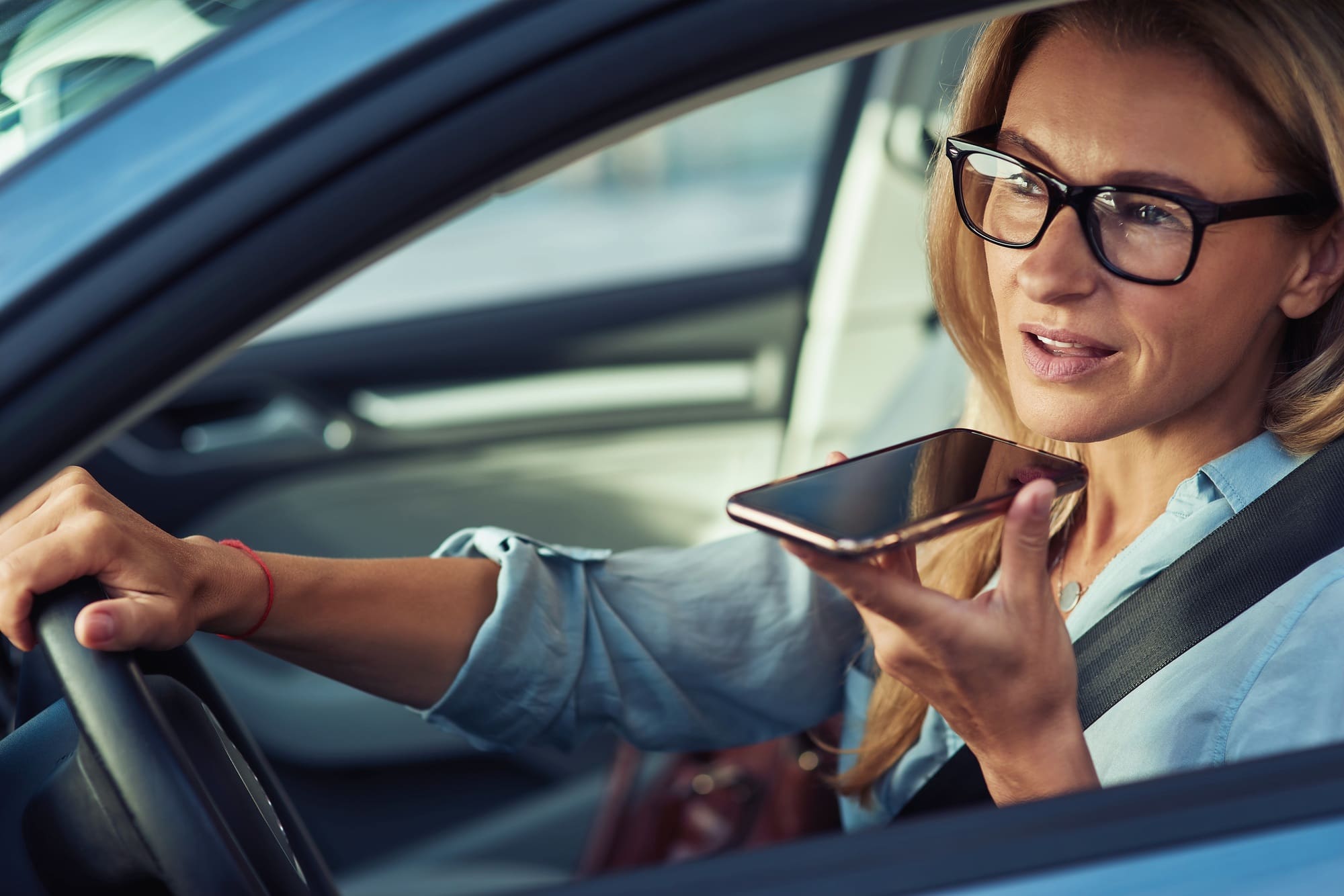 Working on the way to office, busy mature business woman sitting behind steering wheel of her car